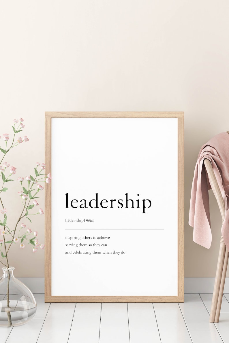 May include: A framed print with the word "leadership" in a bold, black font. The definition of the word is written in a smaller font below, "[lēder-ship] noun inspiring others to achieve serving them so they can and celebrating them when they do."