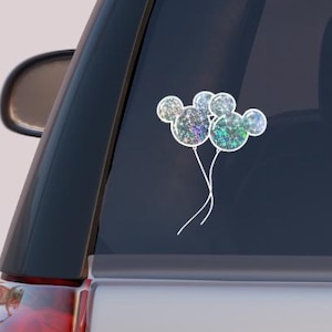 Op de afbeelding: Een autoruit met een sticker van een cluster van iriserende blauwe en groene ballonnen in de vorm van Mickey Mouse-oren.