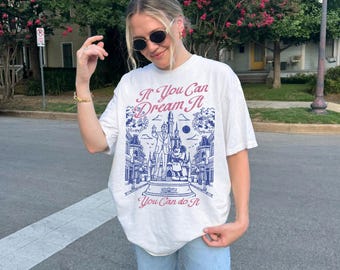May include: White t-shirt with a blue and red graphic featuring a castle, Mickey Mouse, and the text "If You Can Dream It, You Can do It." The shirt has a relaxed fit.