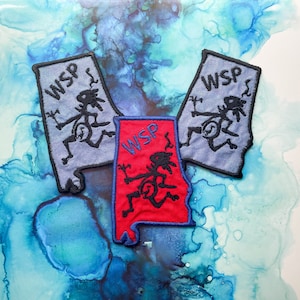 May include: Three embroidered patches in the shape of the state of Alabama. Two are light blue with black stitching, and one is red with black stitching. Each patch features the letters "WSP" and a stylized figure.