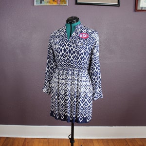 May include: A blue and white patterned dress with long sleeves and a collar. The dress has a gathered waist and a loose fit. The dress has a small red tag with the text "WSP" on it.