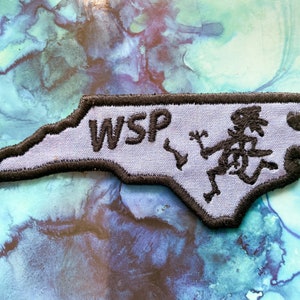 May include: A light blue embroidered patch shaped like the state of North Carolina with the letters "WSP" and a running figure in black.