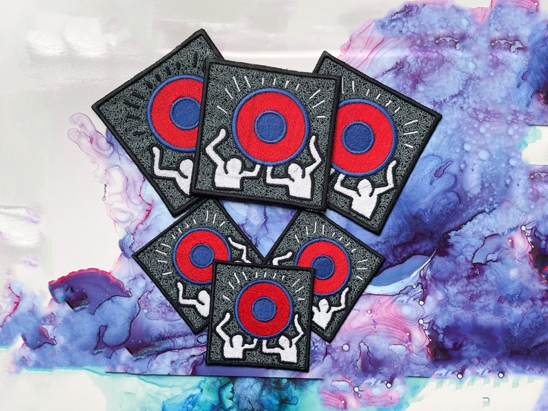 May include: Six gray square patches with embroidered designs. Each patch features two white figures lifting a red and blue circle with radiating lines.