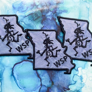 May include: Three gray fabric patches shaped like the state of Missouri with a black outline. Each patch features a stylized black figure dancing and the text "WSP" in black.