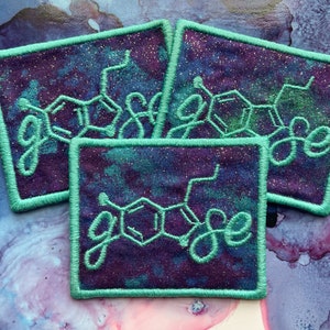 May include: Four teal-colored embroidered patches with a purple and blue galaxy-like background. Each patch features a white embroidered chemical structure with the word "goose" written in cursive.