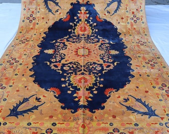 Könnte beinhalten: Ein antiker persischer Teppich mit einem dunkelblauen Mittelteil und einem gold-orangenen floralen Muster. Der Teppich hat einen Fransenrand.