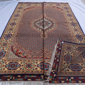 May include: A large, intricately patterned rug with a central medallion in shades of blue, red, and cream. The rug has a fringe border and is folded in half.