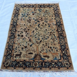 May include: A traditional Persian rug with a beige background and a detailed design of a tree of life with birds and animals. The rug has a dark blue border with intricate floral patterns.