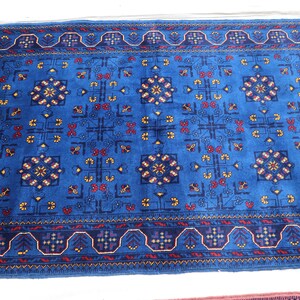 May include: A rectangular area rug featuring a vibrant blue background with a repeating geometric pattern. The design includes stylized floral motifs in red and yellow, framed by a dark blue border with intricate repeating geometric shapes.