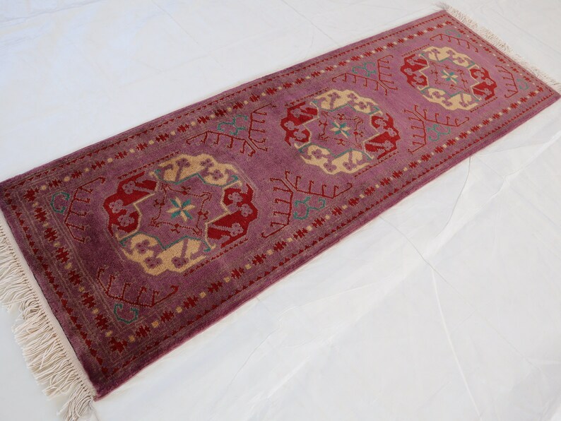 May include: A long, narrow rug with a pink background and a repeating pattern of beige, green, and red floral designs. The rug has fringe on both ends.