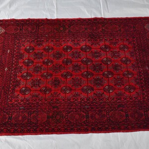 May include: A rectangular, hand-woven rug with a deep red background and intricate black floral patterns. The rug features a central medallion design surrounded by a border with repeating motifs. The rug's dimensions are approximately 3 x 5 feet.