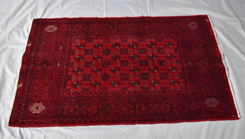 May include: A rectangular, hand-woven rug with a deep red background and intricate black floral patterns. The rug features a central medallion design surrounded by a border with repeating motifs. The rug's dimensions are approximately 3 x 5 feet.