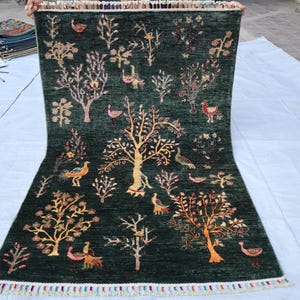 May include: A green rug with a colorful floral and bird design. The rug has a fringe border.
