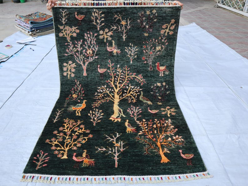 May include: A green rug with a colorful floral and bird design. The rug has a fringe border.