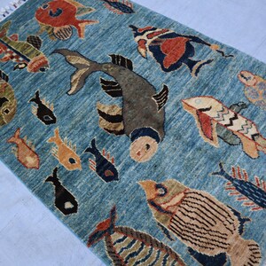 May include: A blue rug with a colorful fish design. The rug features a variety of fish, including a large, gray fish with a black eye, a red fish with a white belly, and a yellow fish with a black tail.