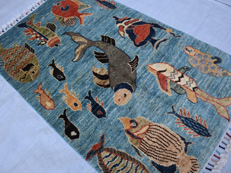 May include: A blue rug with a colorful fish design. The rug features a variety of fish, including a large, gray fish with a black eye, a red fish with a white belly, and a yellow fish with a black tail.