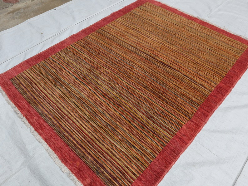 May include: A rectangular rug with a red border and a striped pattern in shades of brown, beige, and black.