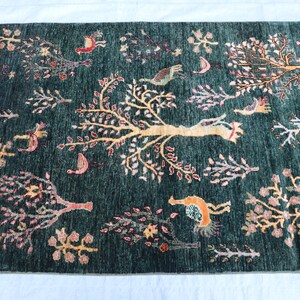 May include: A green rug with a floral pattern featuring trees, birds, and other motifs. The rug has a fringe border.