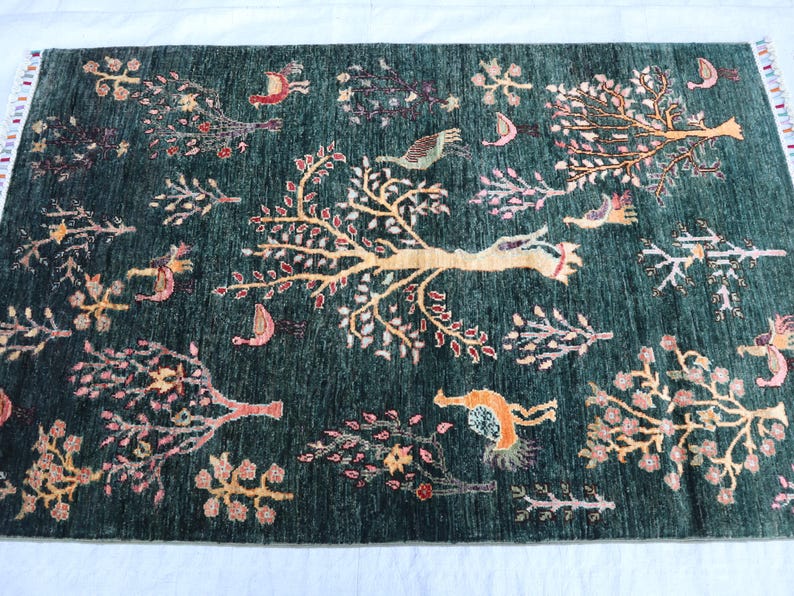 May include: A green rug with a floral pattern featuring trees, birds, and other motifs. The rug has a fringe border.