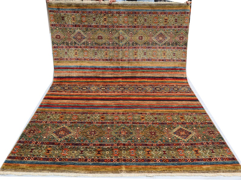 May include: A colorful rug with a geometric pattern in shades of red, orange, yellow, green, blue, and brown. The rug has a fringe border.