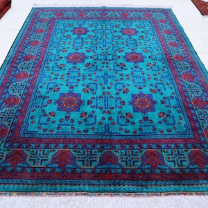 Può includere: Un tappeto rettangolare caratterizzato da un vivace campo turchese con un motivo ripetuto di disegni floreali geometrici blu scuro e rossi. Il tappeto è incorniciato da un'ampia bordura rosso scuro e blu con complessi motivi angolari e frange bianche.