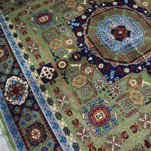 Pu&ograve; includere: Un tappeto con motivi verdi, blu e rossi con disegni intricati. Il tappeto ha un medaglione centrale e un bordo con motivi ripetuti.