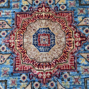 May include: Close-up of a detailed, patterned rug with a central medallion design. The rug features a vibrant color palette of blue, red, beige, and gold. The intricate patterns include geometric shapes and floral motifs, creating a rich, textured appearance.
