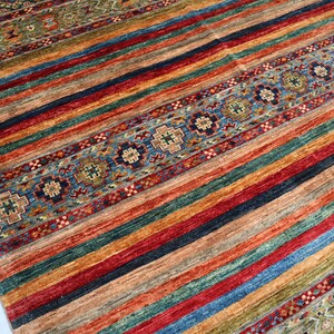 May include: A colorful striped rug with a patterned border. The rug features a variety of colors, including red, blue, green, and yellow. The border is a more intricate design with a blue and white color scheme.