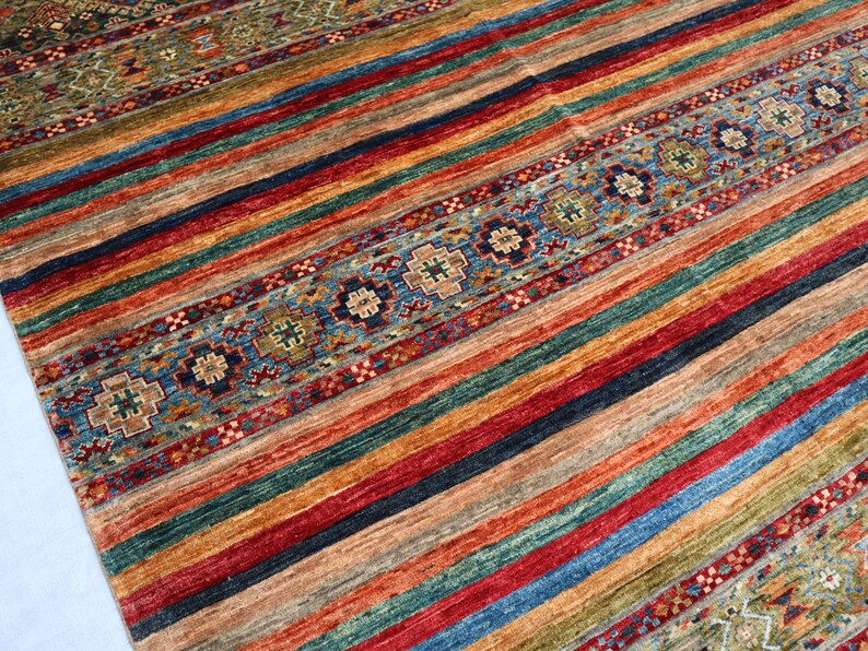 May include: A colorful striped rug with a patterned border. The rug features a variety of colors, including red, blue, green, and yellow. The border is a more intricate design with a blue and white color scheme.
