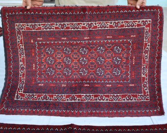 May include: A red and blue patterned rug with a geometric design. The rug has a fringe border and is made of wool.