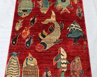 May include: A red rug with a colorful fish design. The rug has a fringe border and is made of wool.