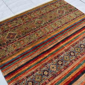 May include: A colorful rug with a geometric pattern. The rug has a mix of red, blue, green, and brown colors. The pattern is made up of stripes and diamonds.