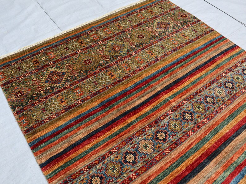 May include: A colorful rug with a geometric pattern. The rug has a mix of red, blue, green, and brown colors. The pattern is made up of stripes and diamonds.