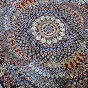 Könnte beinhalten: Ein bunter Teppich mit einem geometrischen Muster, das ein zentrales Medaillon aufweist. Der Teppich hat eine blaue, rote und goldene Farbgebung.