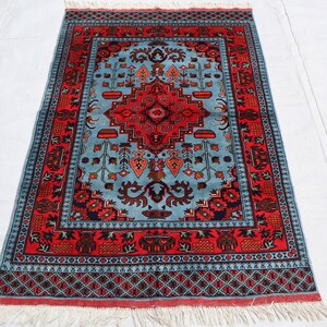 May include: A traditional Persian rug with a blue and red color scheme. The rug features a central medallion with intricate floral and geometric patterns. The border is adorned with a repeating design of stylized flowers and leaves.