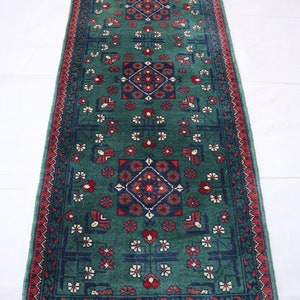 Pu&ograve; includere: Un tappeto da corridoio verde con un designo persiano tradizionale. Il tappeto ha un bordo rosso e intricati motivi floreali in tonalit&agrave; di rosso, blu e crema.