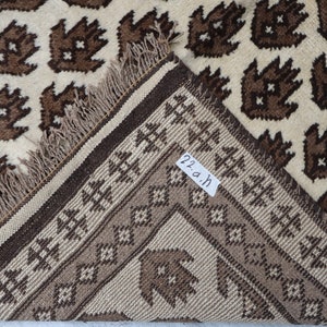 May include: Close-up of the edge of a brown and cream rug with a geometric pattern. The rug has a fringe border and a label that reads "22.a.h".