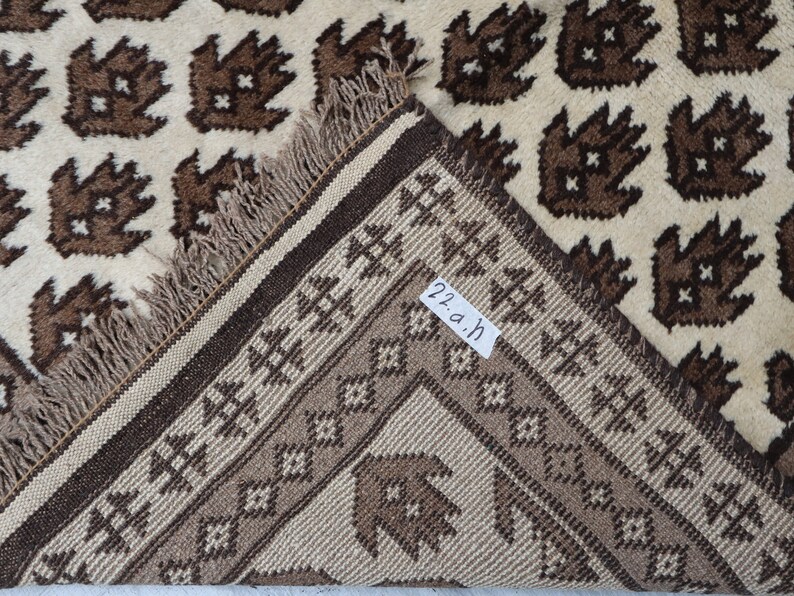 May include: Close-up of the edge of a brown and cream rug with a geometric pattern. The rug has a fringe border and a label that reads "22.a.h".