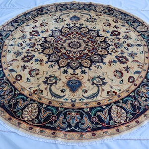 May include: A large round area rug featuring a central medallion design in deep red, navy blue, and cream. The rug displays intricate floral and vine patterns throughout the field, surrounded by a wide navy blue border with repeating floral motifs.