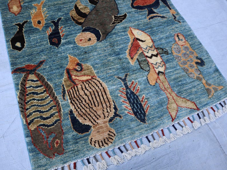 May include: A blue rug with a fringe border features a repeating pattern of stylized fish in various colors and designs. The rug has a vintage, hand-woven aesthetic.