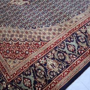Puede incluir: Una alfombra azul, roja y crema con un dise&ntilde;o floral detallado. La alfombra tiene un borde con un patr&oacute;n repetitivo de flores y hojas.