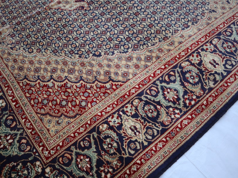 Puede incluir: Una alfombra azul, roja y crema con un dise&ntilde;o floral detallado. La alfombra tiene un borde con un patr&oacute;n repetitivo de flores y hojas.