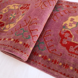 May include: A pink rug with a traditional Persian design featuring intricate patterns in shades of red, yellow, and green.