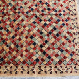 May include: A beige rug with a diamond pattern in shades of red, blue, green, and cream. The rug has a fringe border.