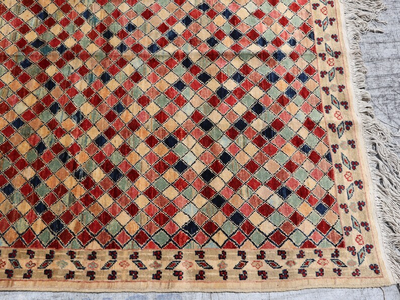 May include: A beige rug with a diamond pattern in shades of red, blue, green, and cream. The rug has a fringe border.