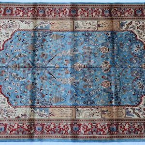 May include: A blue and red patterned rug with a floral design. The rug has a border with a repeating pattern of stylized flowers and leaves.
