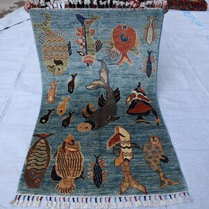 May include: A blue rug with a fringe border features a repeating pattern of colorful fish. The rug has a light blue background with a darker blue pattern.