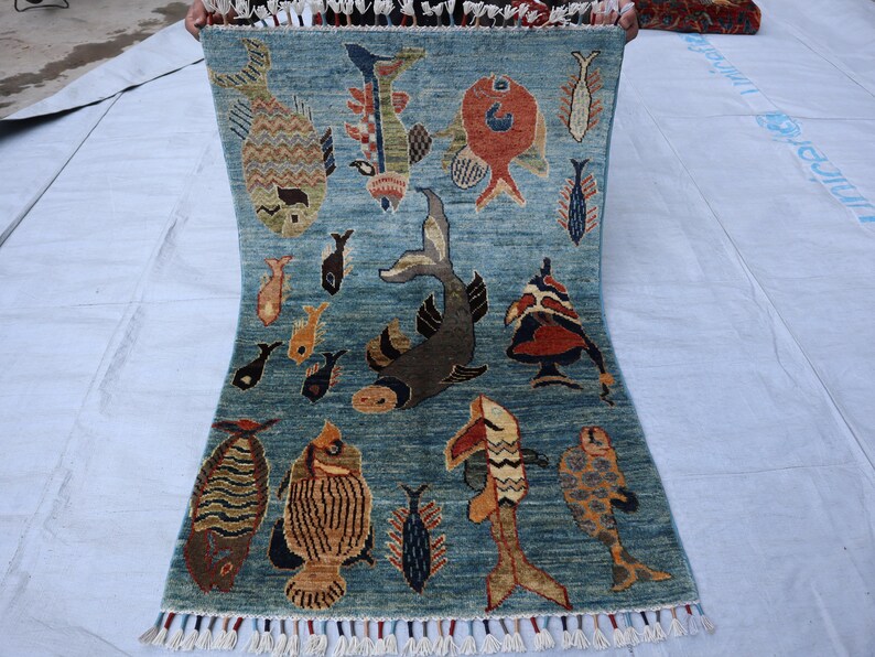 May include: A blue rug with a fringe border features a repeating pattern of colorful fish. The rug has a light blue background with a darker blue pattern.