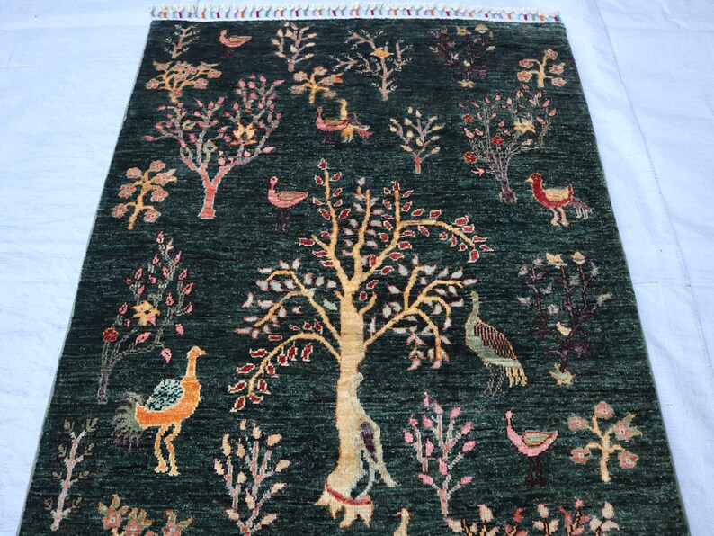 May include: A green rug with a repeating pattern of trees, birds, and flowers. The rug has a fringed edge.