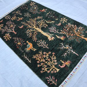 May include: A green rug with a colorful floral and bird design. The rug has a fringe border.